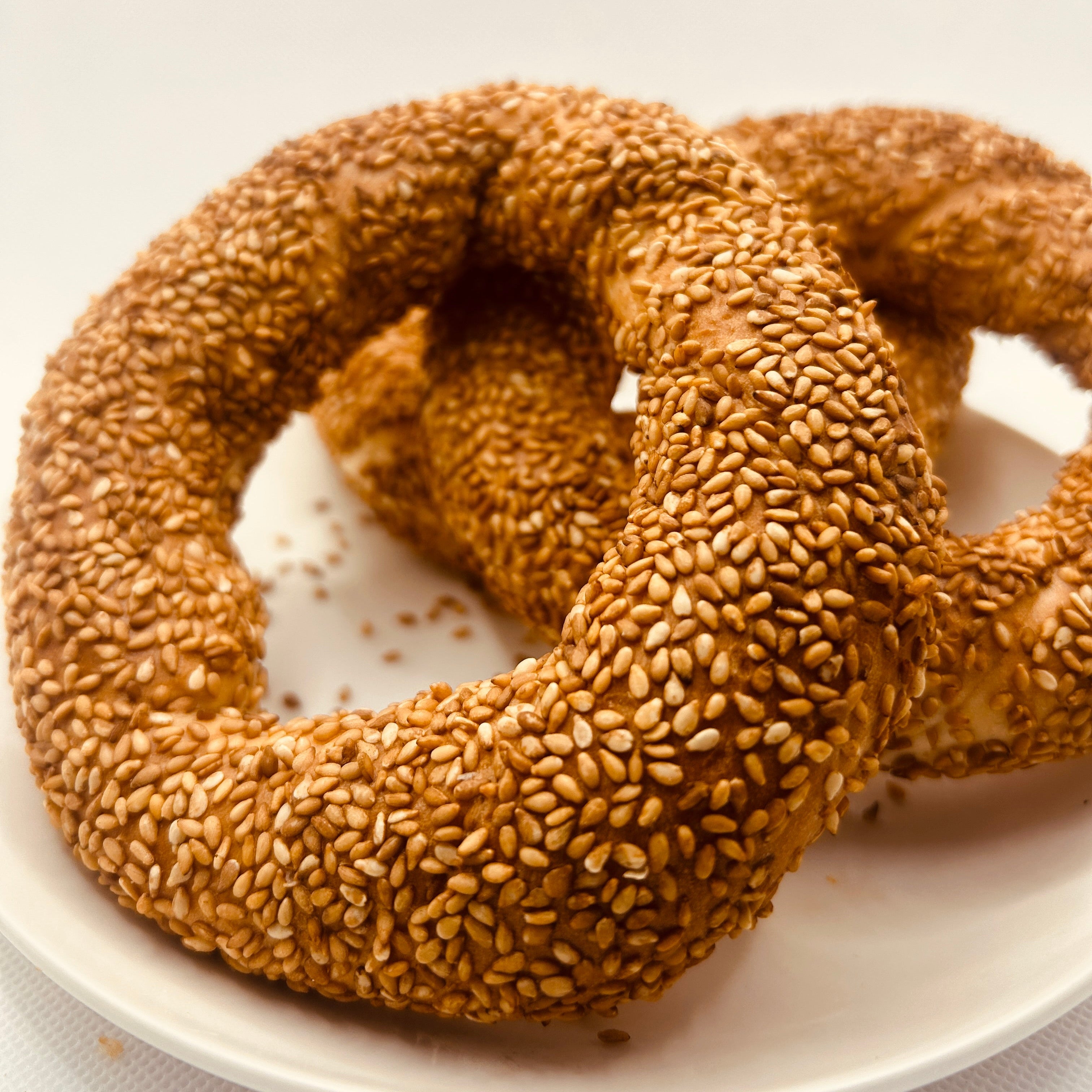 Two sesame seed bagels on a white plate with a white background