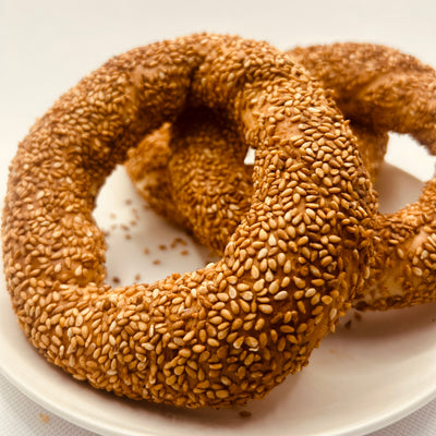 Two sesame seed bagels on a white plate with a white background
